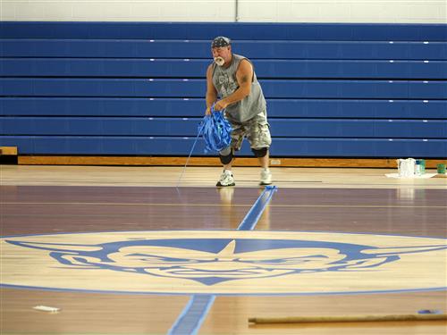 Worker removes tape from gym floor 