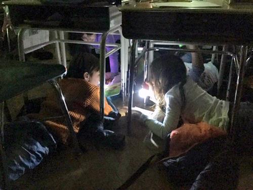 Students read under desks in dark with flashlights 