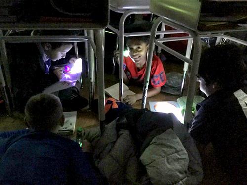 Students read under desks in dark with flashlights 