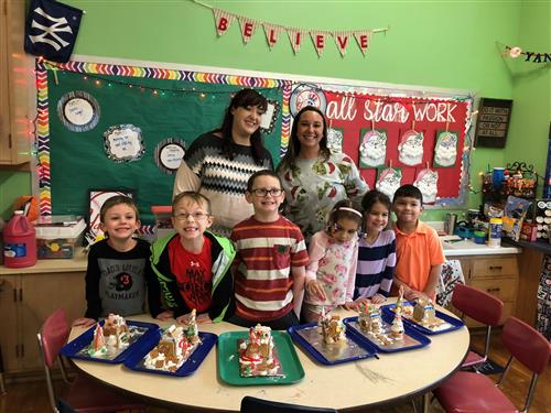 Students/staff pose with gingerbread house creations 