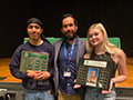  two students and a teacher pose with plaques inside an auditorium