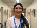  woman smiles at the camera wearing a white sweater and a black head scarf