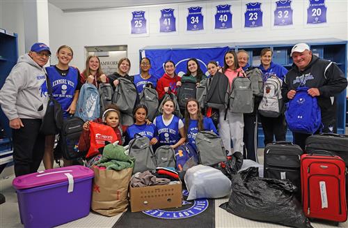 basketball team poses with backpacks and bins/suitcases of donated clothing and items.