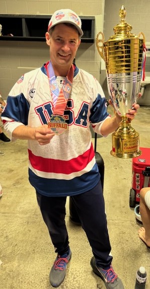 man poses with a trophy, medal, and USA jersey