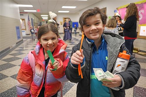 Two students hold of colored strips of paper they bought with quarters