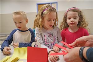 three students get colored strips of paper from a table