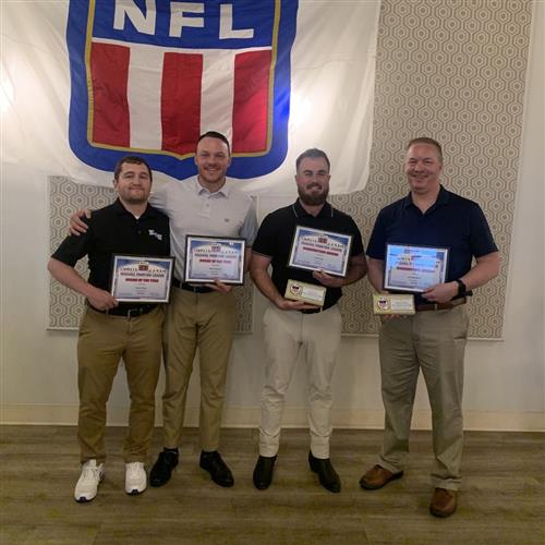 four men stand with awards in front of an NFL flag