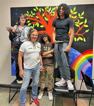 students and teacher pose in front of a mural they're painting