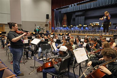 students sit and play instruments for a concert rehearsal