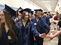  students walk in their caps and gowns and high five younger students in a hallway