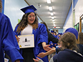  student in cap and gown high fives younger students in a hallway