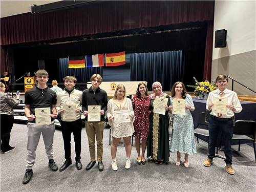 World Language students stand in a line holding up honors certificates