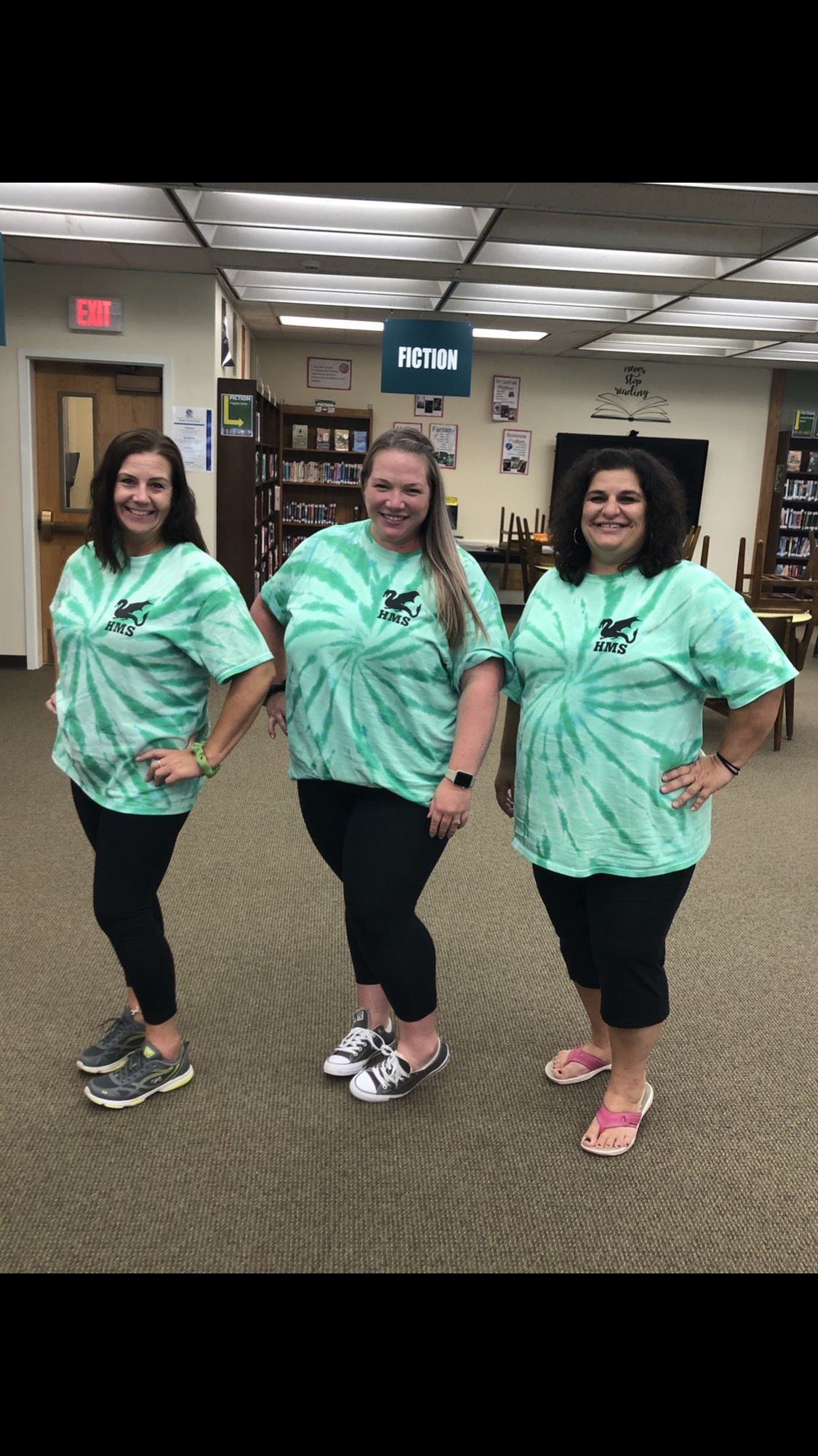 Three teachers in the library wearing green tie dye shirts